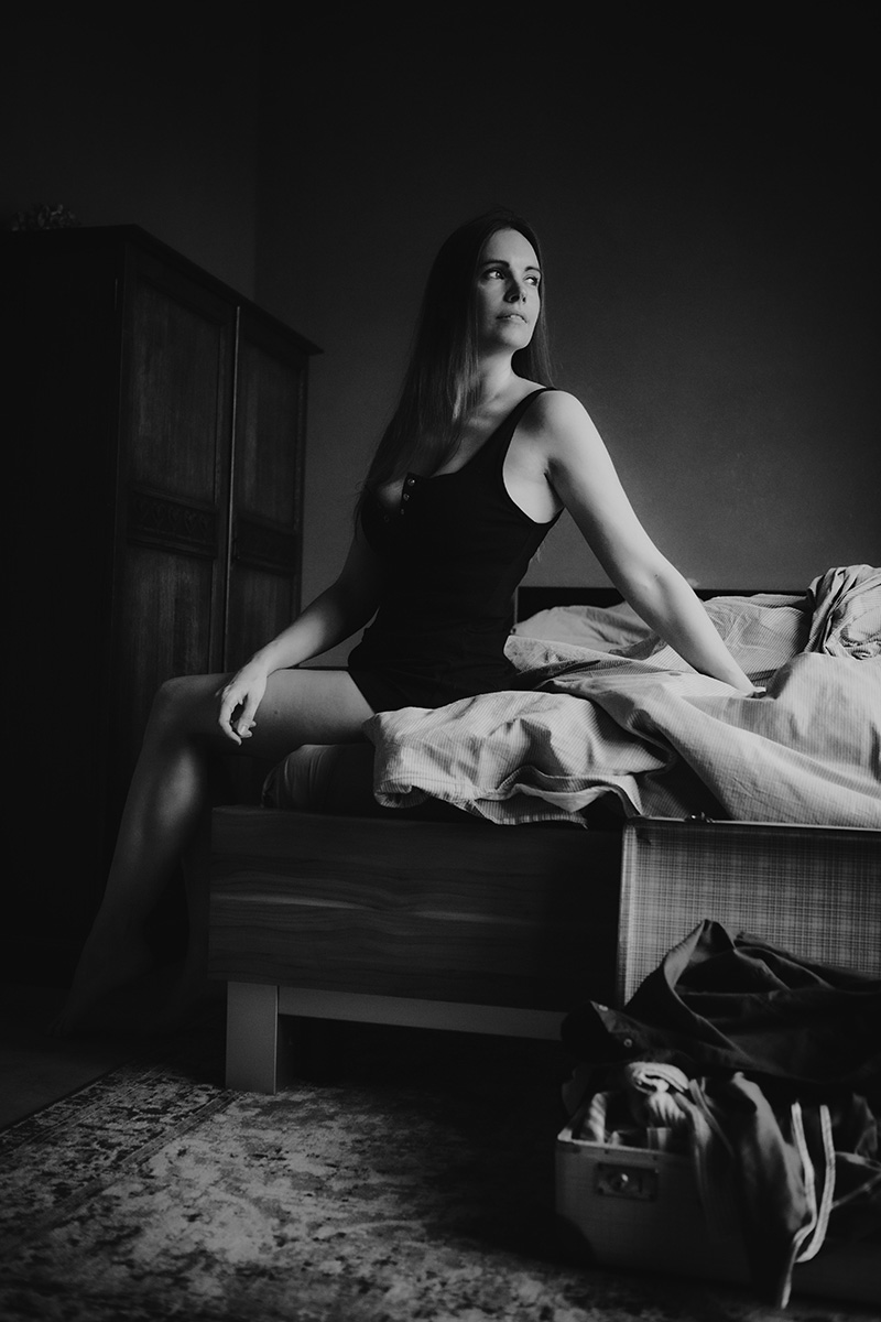 Zwart-wit boudoirportret van een vrouw zittend in een sfeervolle kamer.